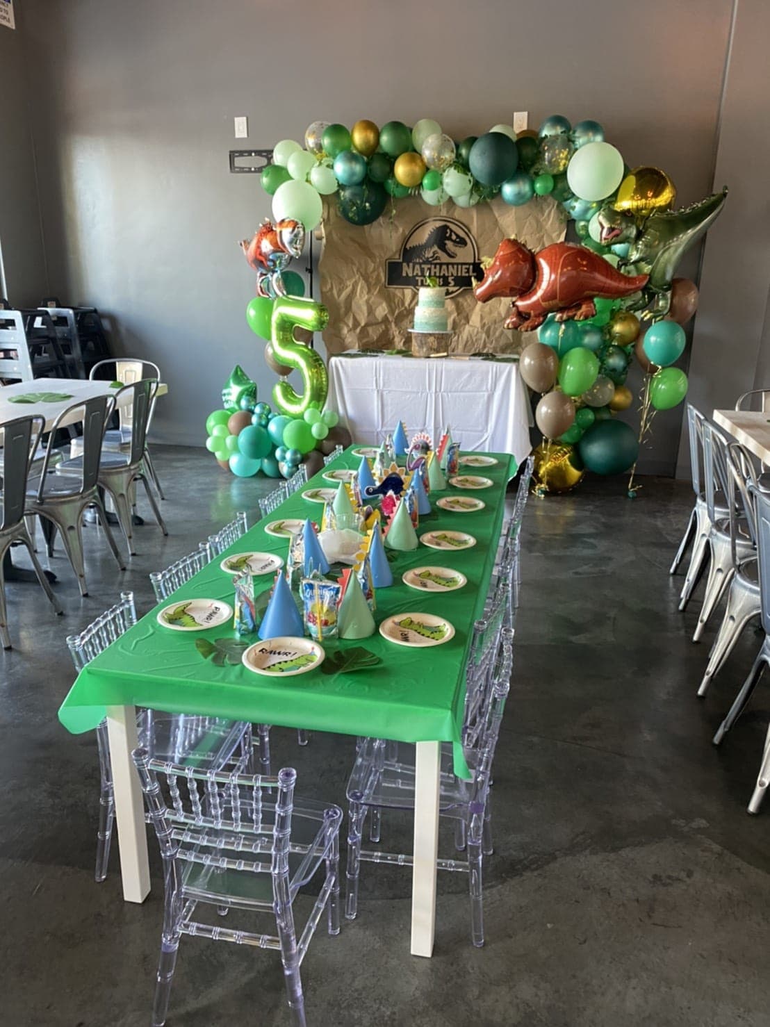Table d’anniversaire dinosaure verte avec assiettes, ballons et décorations à thème