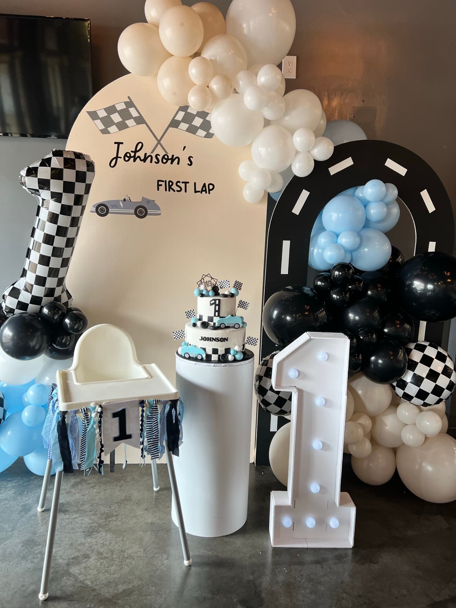 Décor de premier anniversaire automobile noir, blanc et bleu avec ballons et chiffre un lumineux