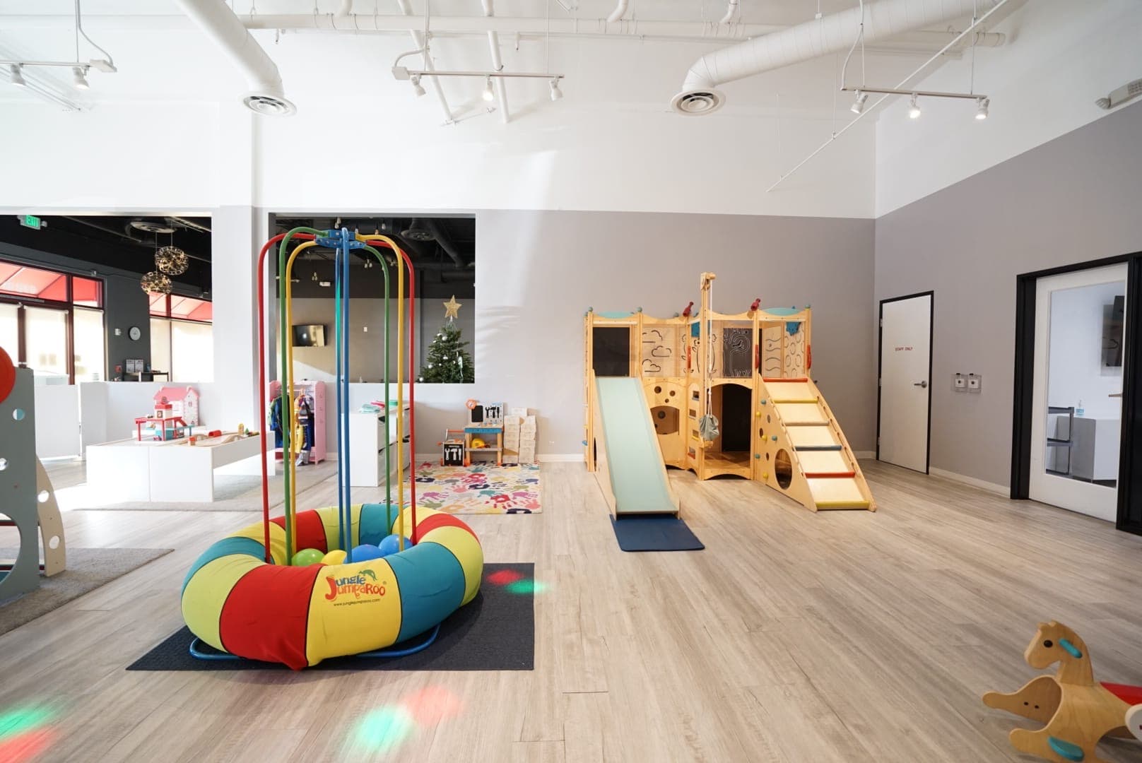 Wide view of the bright indoor playground with wooden slides and activity tables