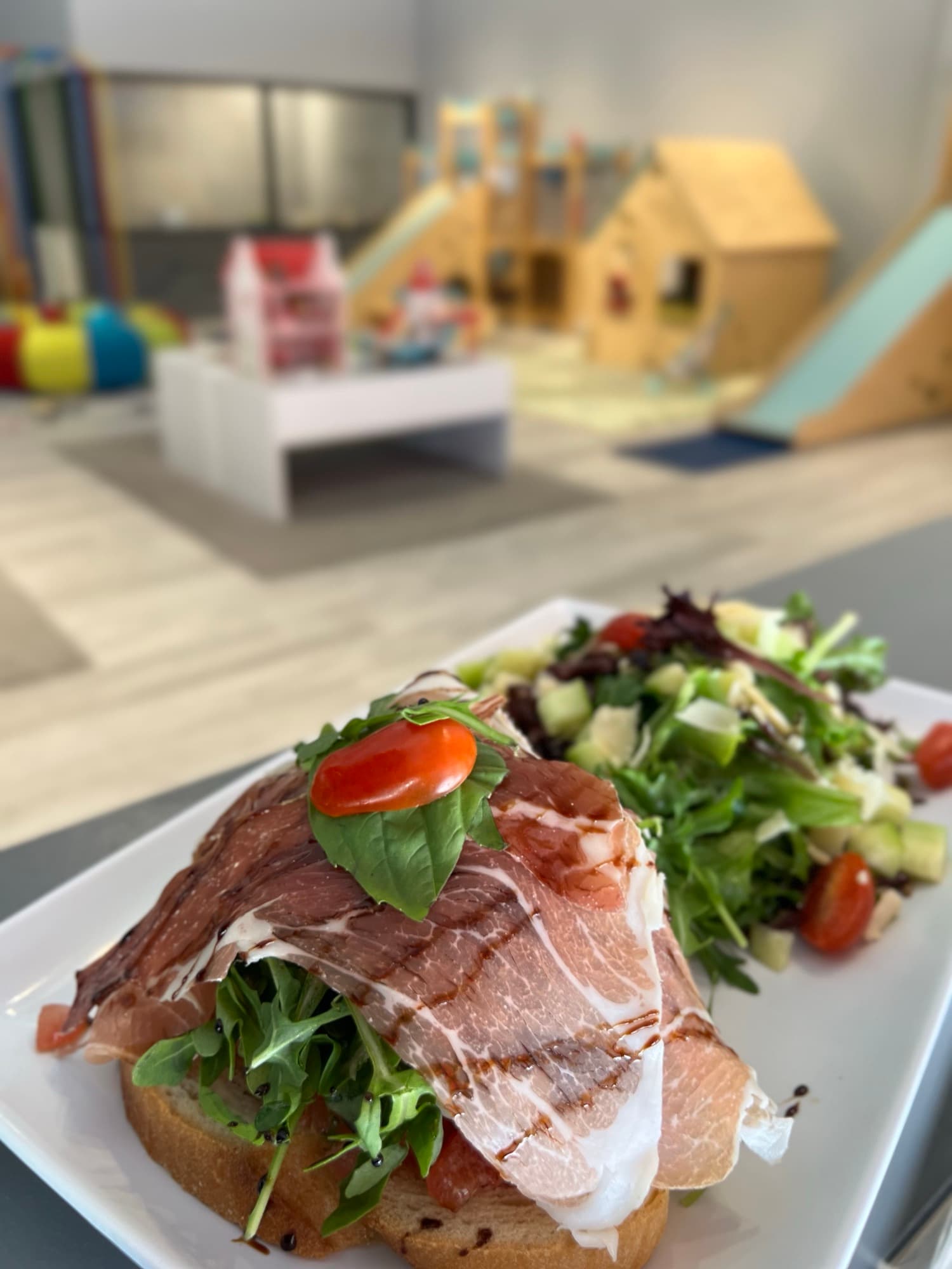 Open-faced café sandwich and salad served beside the softly focused indoor playground