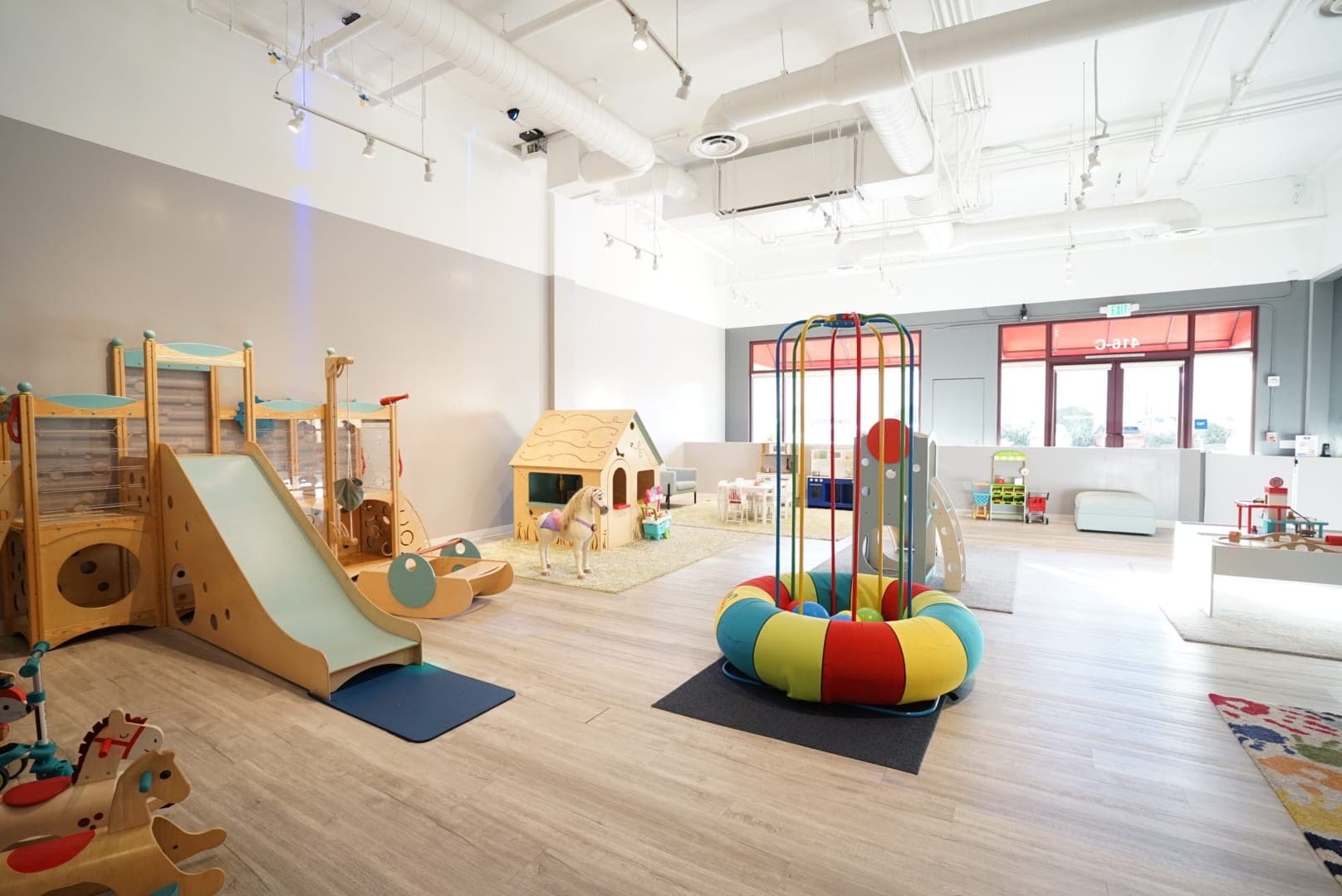 Wide view of the bright indoor playground with wooden play structures and a colorful carousel