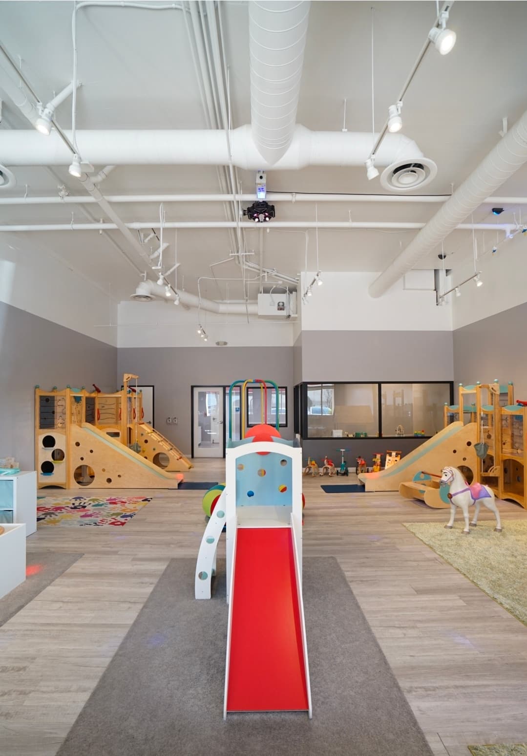 Red toddler slide centered between the wooden climbing structures in the My Little Paris indoor playground